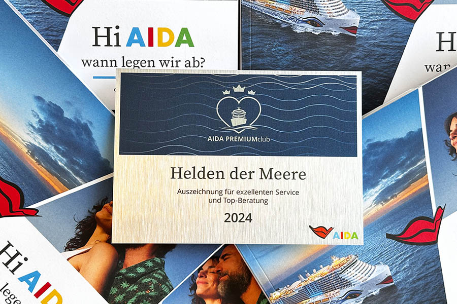 Urkunde ‚AIDA PREMIUMclub – Helden der Meere 2024‘, verliehen an Kozica Reisen für exzellenten Service und Top-Beratung, umgeben von AIDA Werbematerialien.