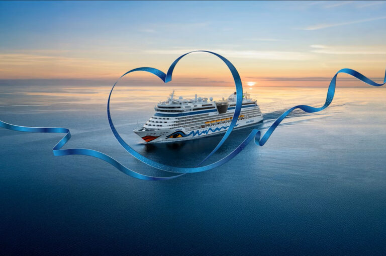 Kreuzfahrtschiff AIDAluna auf dem Meer bei Sonnenuntergang, eingerahmt von einem großen, blauen Band in Herzform.