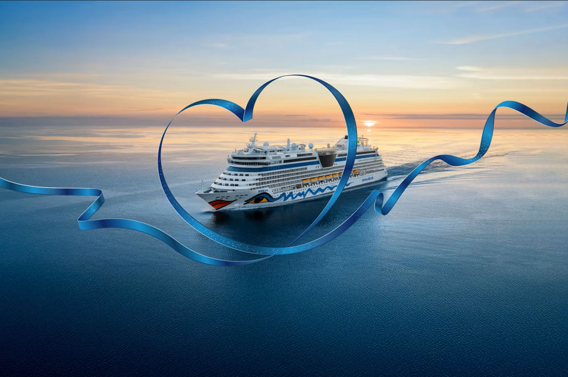 Kreuzfahrtschiff AIDAluna auf dem Meer bei Sonnenuntergang, eingerahmt von einem großen, blauen Band in Herzform.