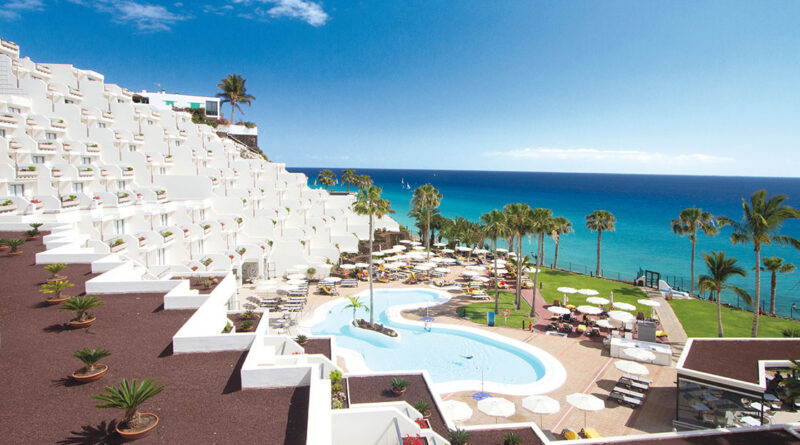 Blick auf das frisch renovierte Hotel Riu Palace Calypso auf Fuerteventura mit weißer Architektur, Poollandschaft, Palmen und Meer im Hintergrund.