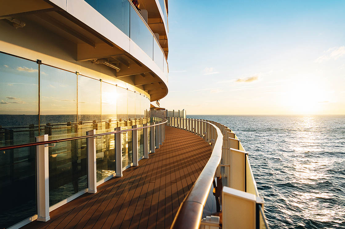 Sonnenuntergang über dem Meer, gesehen vom Außendeck eines Kreuzfahrtschiffs mit Glasgeländer.