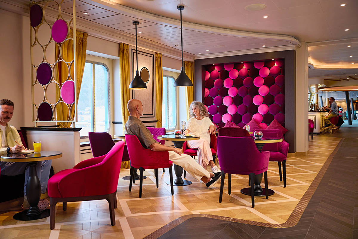 Modernisierte French Kiss Bar auf der AIDAbella mit roten Sesseln und gemütlichen Sitzgruppen.
